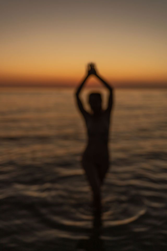 Silhouette au bord de l'eau, bras levés, lumière du soir